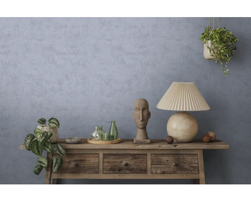 Buffet rustique en bois devant un mur bleu-gris texturé avec une lampe de table, une sculpture en pierre, des bouteilles en verre et des plantes.