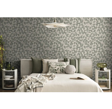 Modernes Schlafzimmer mit Vliestapete mit Blattmuster, Bett mit verschiedenen Kissen und dekorativen Beistelltischen in Naturtönen.