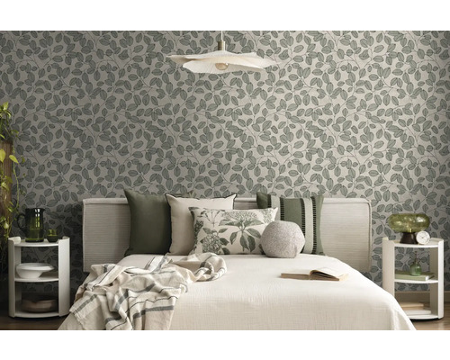 Modernes Schlafzimmer mit Vliestapete mit Blattmuster, Bett mit verschiedenen Kissen und dekorativen Beistelltischen in Naturtönen.
