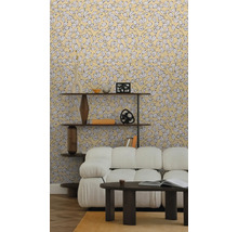 Papier peint intissé à motif de feuilles jaunes dans un salon clair avec canapé blanc, table basse sombre et étagère en bois sur parquet.