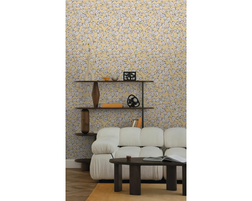 Papier peint intissé à motif de feuilles jaunes dans un salon clair avec canapé blanc, table basse sombre et étagère en bois sur parquet.
