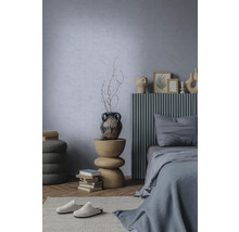 Chambre moderne avec mur bleu clair texturé, lit avec tête de lit à lattes grises et table d'appoint sculpturale en bois.