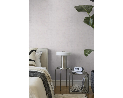 Modernes Schlafzimmer mit hellvioletter Strukturtapete, Metalllampe auf einem Hocker und einer großen grünen Zimmerpflanze.