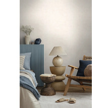 Chambre à coucher moderne avec un fauteuil en bois, une table de chevet sculpturale, une lampe avec abat-jour plissé et un lit avec panneau bleu.