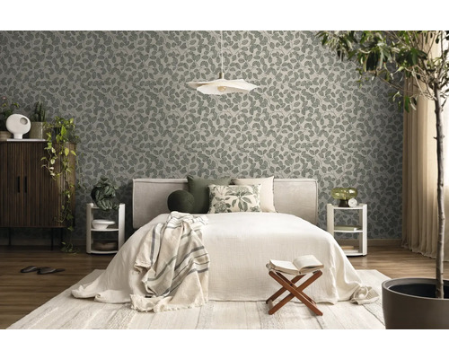 Vliestapete mit Blattmuster in einem hellen Schlafzimmer mit Bett, Holzmöbeln und Zimmerpflanzen.