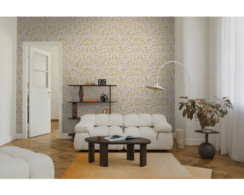 Salon avec papier peint jaune à motifs de feuilles, canapé blanc, table basse foncée et parquet. Ambiance lumineuse et moderne.