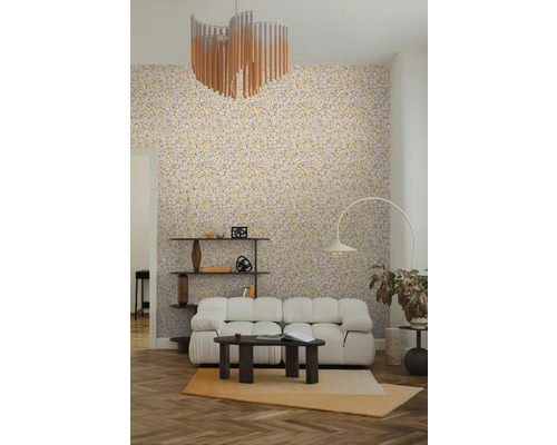 Salon clair et organisé avec papier peint à motif de feuilles, canapé modulable blanc, table basse foncée, lampadaire arqué et étagère en bois.