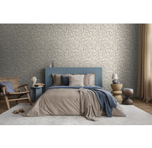 Helles Schlafzimmer mit Blattmuster-Tapete, Bett mit blauem Lamellen-Kopfteil, beigem Bettzeug und Holzmöbeln auf einem hellen Teppich.