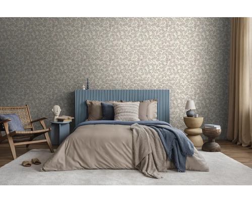 Helles Schlafzimmer mit Blattmuster-Tapete, Bett mit blauem Lamellen-Kopfteil, beigem Bettzeug und Holzmöbeln auf einem hellen Teppich.