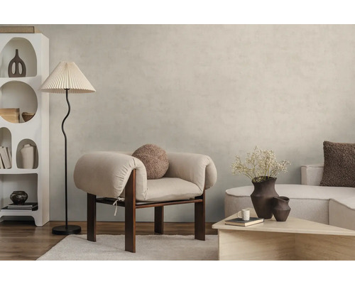 Salon moderne avec peinture murale beige clair effet béton, fauteuil clair, lampadaire et étagère blanche sur parquet.