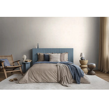 Chambre moderne avec tête de lit bleue cannelée, literie beige, fauteuil en bois et tapis clair devant un mur gris clair.