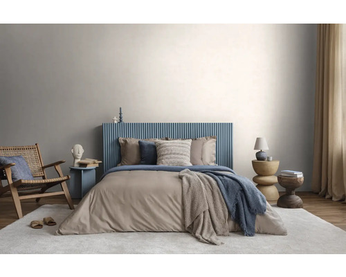 Chambre moderne avec tête de lit bleue cannelée, literie beige, fauteuil en bois et tapis clair devant un mur gris clair.