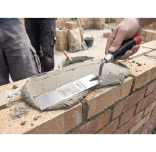 Une main étale du mortier sur un mur en briques à l'aide d'une truelle de maçon sur un chantier.