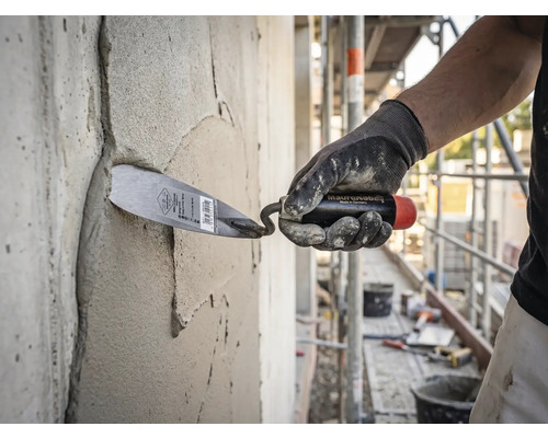 Ein Handwerker trägt mit einer Maurerkelle Mörtel auf eine Betonwand auf einer hellen und organisierten Baustelle auf.