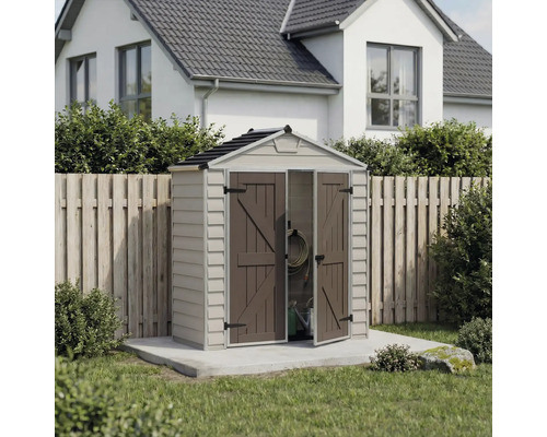 Petit abri de jardin en plastique avec toit à pignon et double porte ouverte, installé sur une dalle en béton devant une clôture en bois.