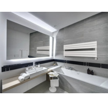 Salle de bain moderne avec carrelage gris, grand miroir éclairé, lavabo blanc, baignoire et radiateur sèche-serviettes horizontal.