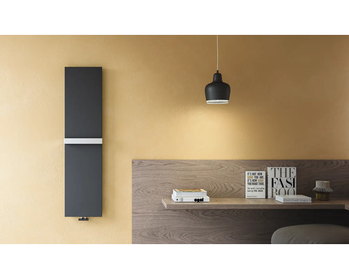 Radiateur design vertical gris foncé avec porte-serviette blanc sur un mur jaune à côté d'un bureau en bois.