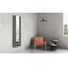 Radiateur design vertical avec miroir intégré dans un salon moderne avec murs en béton, fauteuil en cuir et mobilier minimaliste.