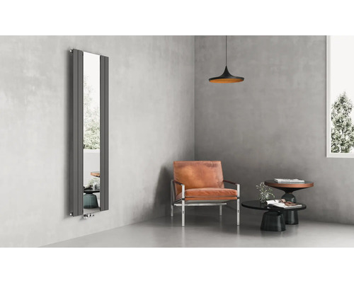 Radiateur design vertical avec miroir intégré dans un salon moderne avec murs en béton, fauteuil en cuir et mobilier minimaliste.