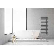 Salle de bains moderne et lumineuse avec baignoire en îlot blanche, radiateur sèche-serviettes anthracite sur mur aspect béton et tabouret en bois.