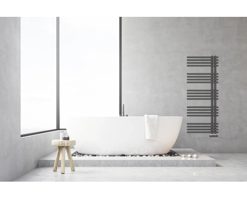 Salle de bains moderne et lumineuse avec baignoire en îlot blanche, radiateur sèche-serviettes anthracite sur mur aspect béton et tabouret en bois.