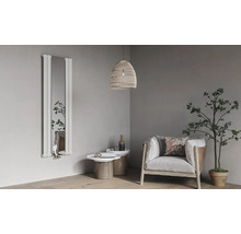 Radiateur design vertical avec miroir intégré dans un salon moderne et lumineux avec fauteuil, tables d'appoint et plante d'intérieur.