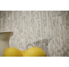 Papier peint intissé avec motif de pierre texturé en gris et beige et une silhouette de carafe discrète.