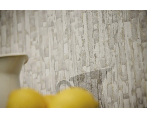 Papier peint intissé avec motif de pierre texturé en gris et beige et une silhouette de carafe discrète.
