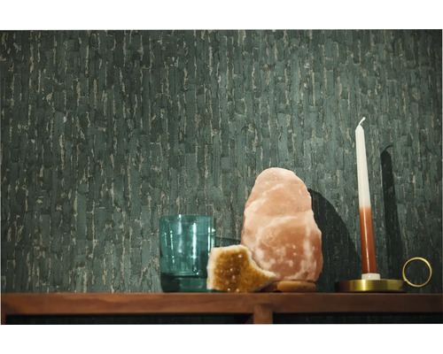 Papier peint intissé vert foncé avec une structure verticale sur un mur derrière une étagère en bois avec une lampe à sel une bougie et un verre.