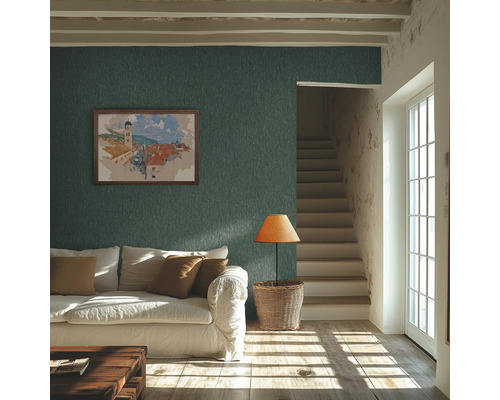 Salon rustique avec papier peint texturé bleu pétrole, canapé blanc, escalier en bois et lumière naturelle par une fenêtre à croisillons.