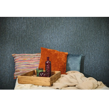 Papier peint bleu texturé dans une pièce avec des coussins décoratifs orange, bleus et multicolores, un plateau en bois et un plaid tricoté.