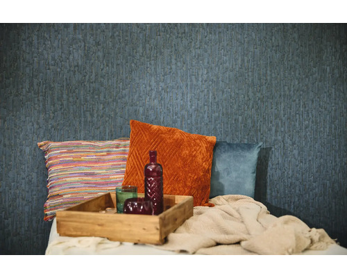 Papier peint bleu texturé dans une pièce avec des coussins décoratifs orange, bleus et multicolores, un plateau en bois et un plaid tricoté.