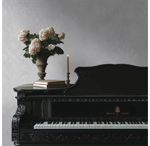 Piano à queue noir sculpté devant un mur texturé gris clair, décoré d'un vase d'hortensias, de livres et d'une bougie.