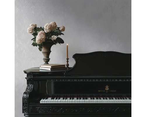 Piano à queue noir sculpté devant un mur texturé gris clair, décoré d'un vase d'hortensias, de livres et d'une bougie.