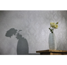 Papier peint intissé à motif ornemental discret et texture, avec un vase de roses devant sur une surface en bois.