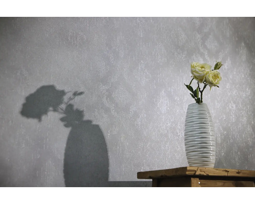 Papier peint intissé à motif ornemental discret et texture, avec un vase de roses devant sur une surface en bois.