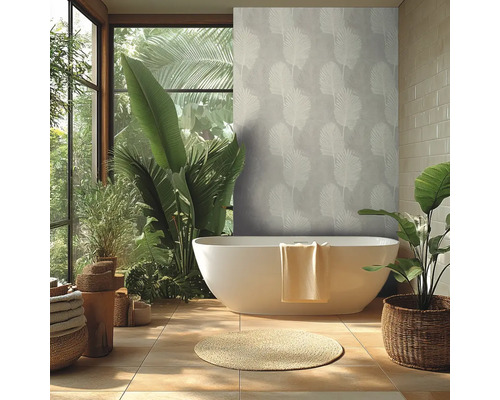 Salle de bains moderne et lumineuse avec baignoire en ilot, papier peint intisse au motif tropical, grandes plantes et carrelage.