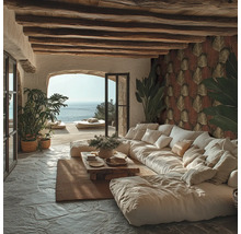 Rustikales Wohnzimmer mit großem weißem Sofa, Natursteinboden und Holzbalkendecke. Eine Wand ist mit gemusterter Tapete mit Blattmotiven gestaltet.