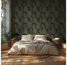 Chambre avec papier peint foncé à motif de feuilles, lit clair, tapis tressé, parquet et plantes d’intérieur sous une lumière vive.
