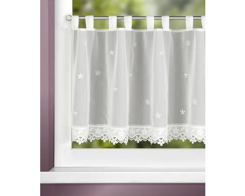 Brise-bise transparent à pattes avec broderies de fleurs et bordure en dentelle fleurie sur une fenêtre.