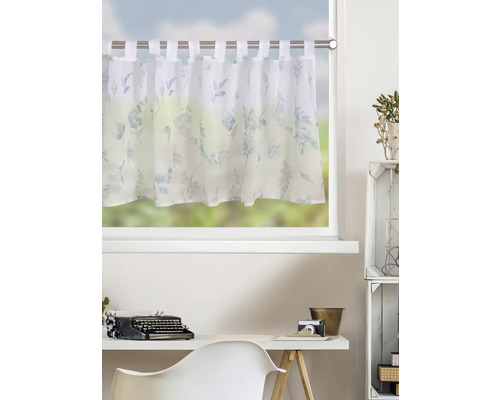 Rideau brise-bise court à pattes avec motif floral bleu on tissu blanc, monté sur une tringle au-dessus d'un bureau dans une pièce claire.