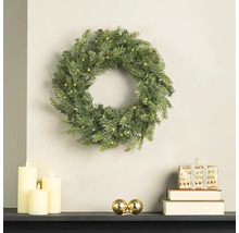 Couronne de Noël artificielle avec éclairage LED au mur, décorée de bougies, de boules et de cadeaux sur une cheminée.