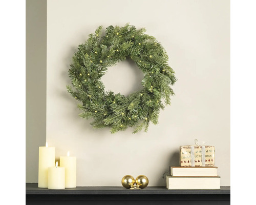 Couronne de Noël artificielle avec éclairage LED au mur, décorée de bougies, de boules et de cadeaux sur une cheminée.
