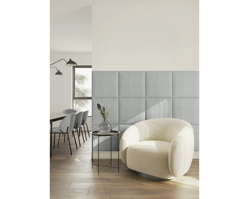 Salon moderne et lumineux avec des panneaux muraux carrés rembourrés en tissu bleu clair à côté d un fauteuil rond en tissu bouclé blanc.