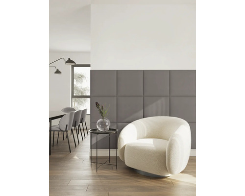 Salon moderne avec panneaux muraux rembourrés gris, fauteuil clair et coin repas à l arrière-plan.