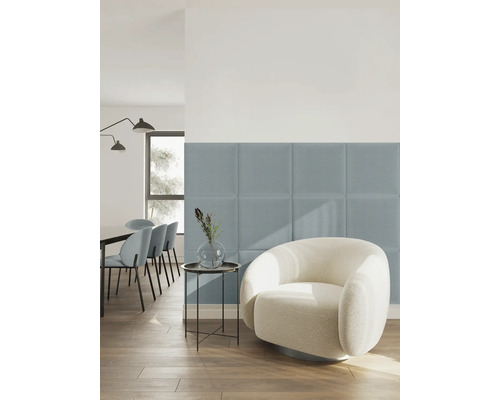 Panneaux muraux rembourrés carrés en tissu bleu dans un salon lumineux de style moderne avec un fauteuil blanc et un parquet en bois.