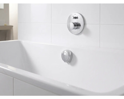 Unterputz-Badearmatur und Überlaufgarnitur aus Chrom an einer weißen Badewanne in einem hellen, organisierten Badezimmer.