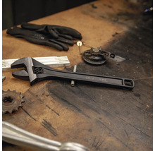 Clé à molette réglable en chrome-vanadium sur un établi à côté d'outils et de gants de travail.