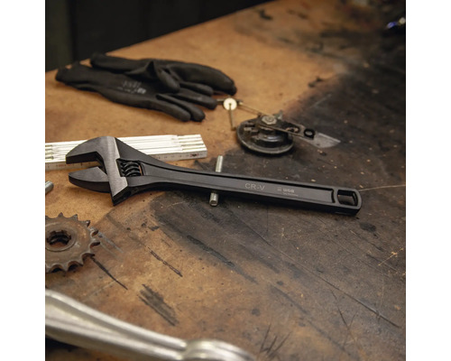 Clé à molette réglable en chrome-vanadium sur un établi à côté d'outils et de gants de travail.