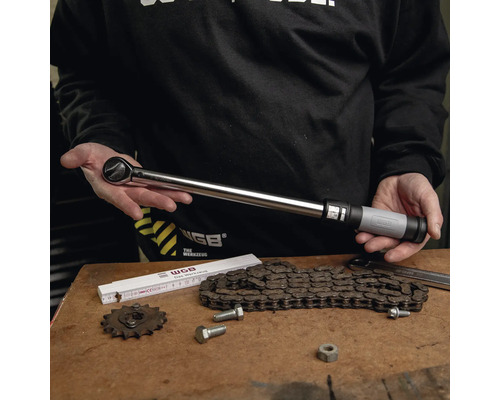 Clé dynamométrique métallique avec poignée réglable, présentée par une personne sur un établi avec une chaîne et des outils.